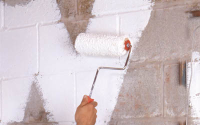 Applying waterproofing paint to a basement wall