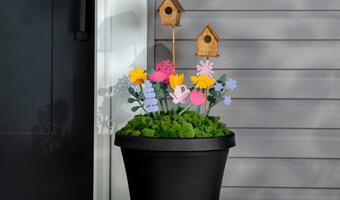 A black planter filled with greenery, painted wooden flowers and small, wood stained bird houses. The planter is on a front porch to the right of the front door. 