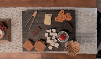 Stained wood charcuterie board covered with crackers, cheese, pretzels, mashmallows and chocolate.